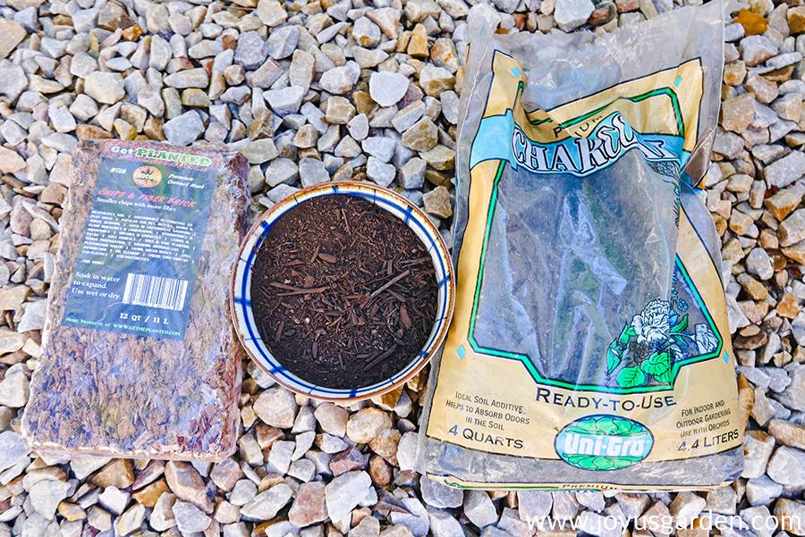 coco fiber in a block a bowl of compost & a bag of charcoal lay on a pebble walkway